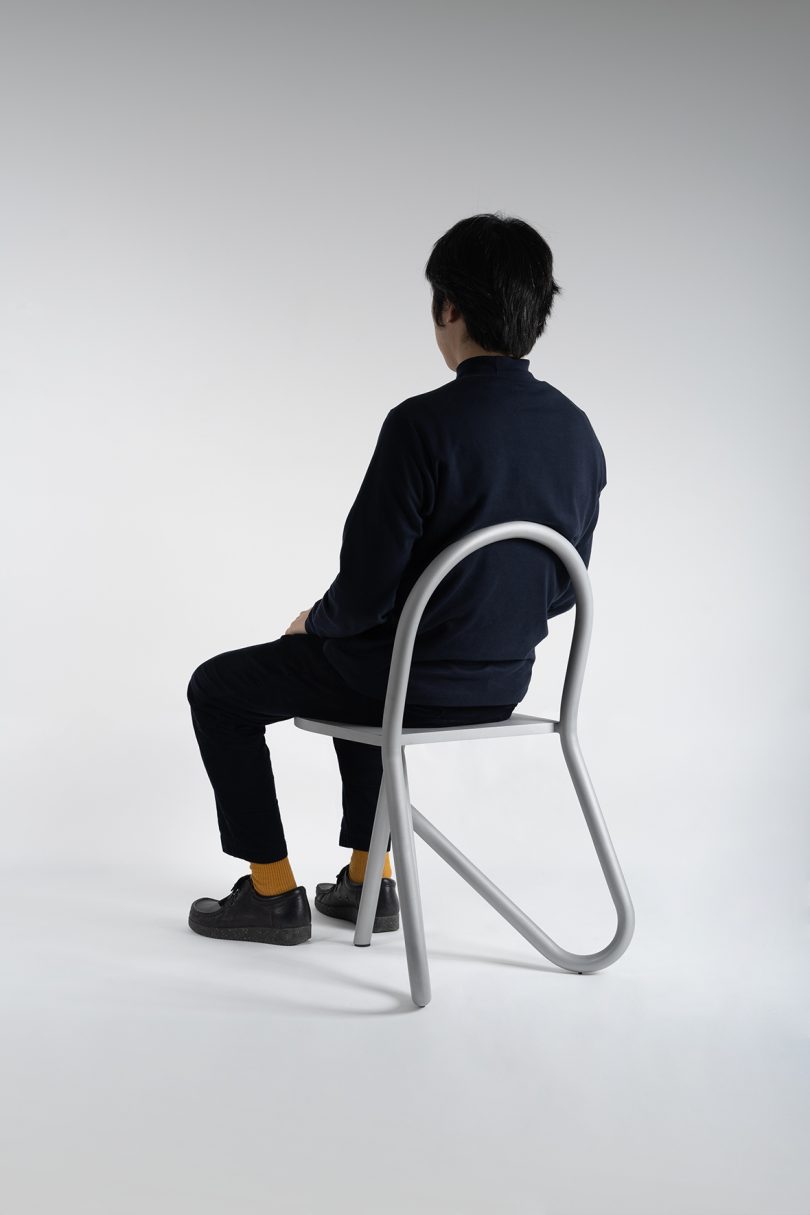 man wearing all black and sitting in profile of tubular chair