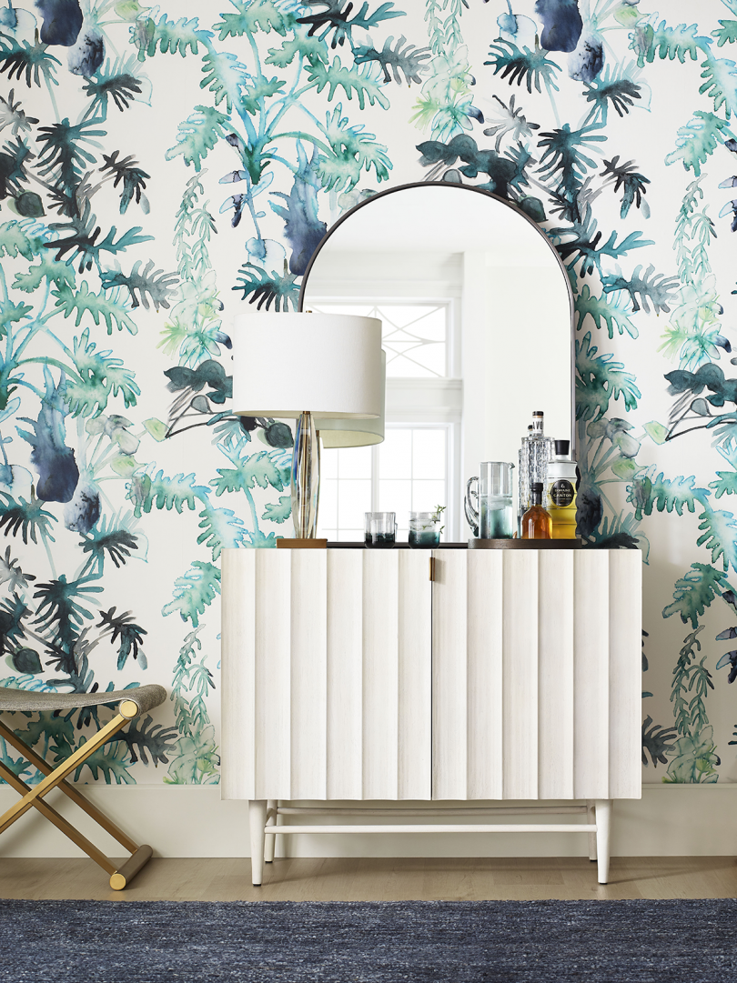 credenza and mirror in front of wall with wallpaper featuring abstract leaves