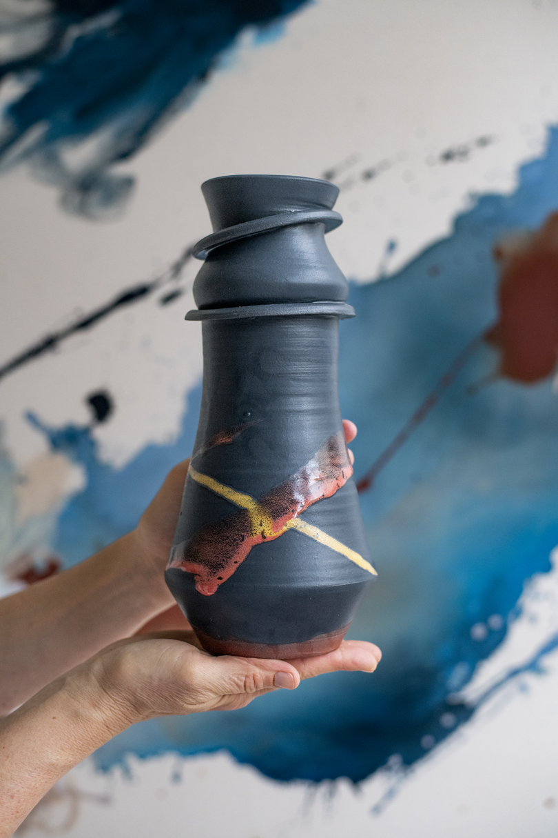 slim black ceramic vase with veining being held by two hands
