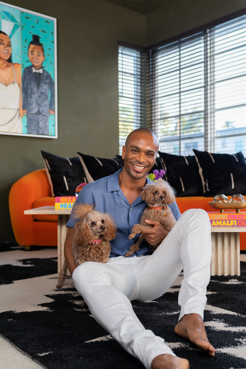 brown-skinned man in blue shirt and white pants with two dogs