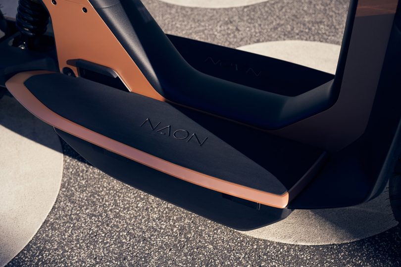 Detail of scooter's floorboard foot platform where batteries are stored underneath, imprinted with NAON logo.