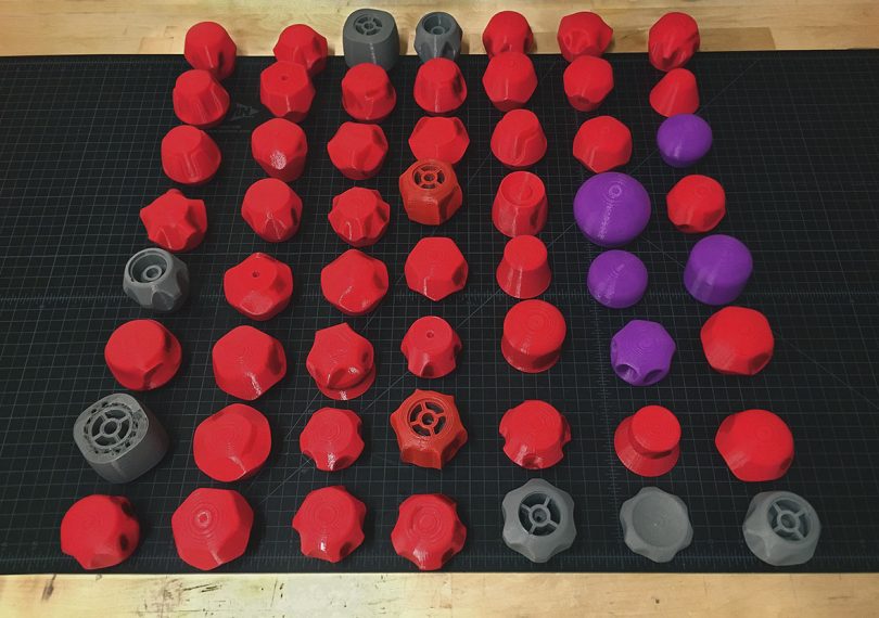 A table filled with 3D-printed red plastic knob model designs.