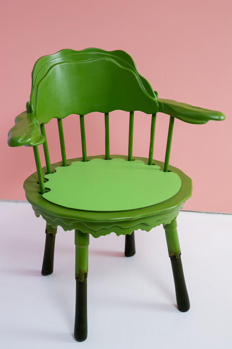 green wooden armchair on white floor in front of light pink wall