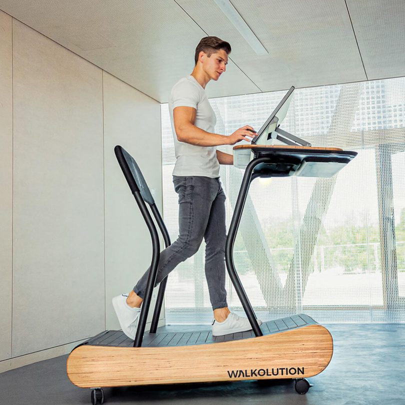 man walking on treadmill workstation while working on laptop