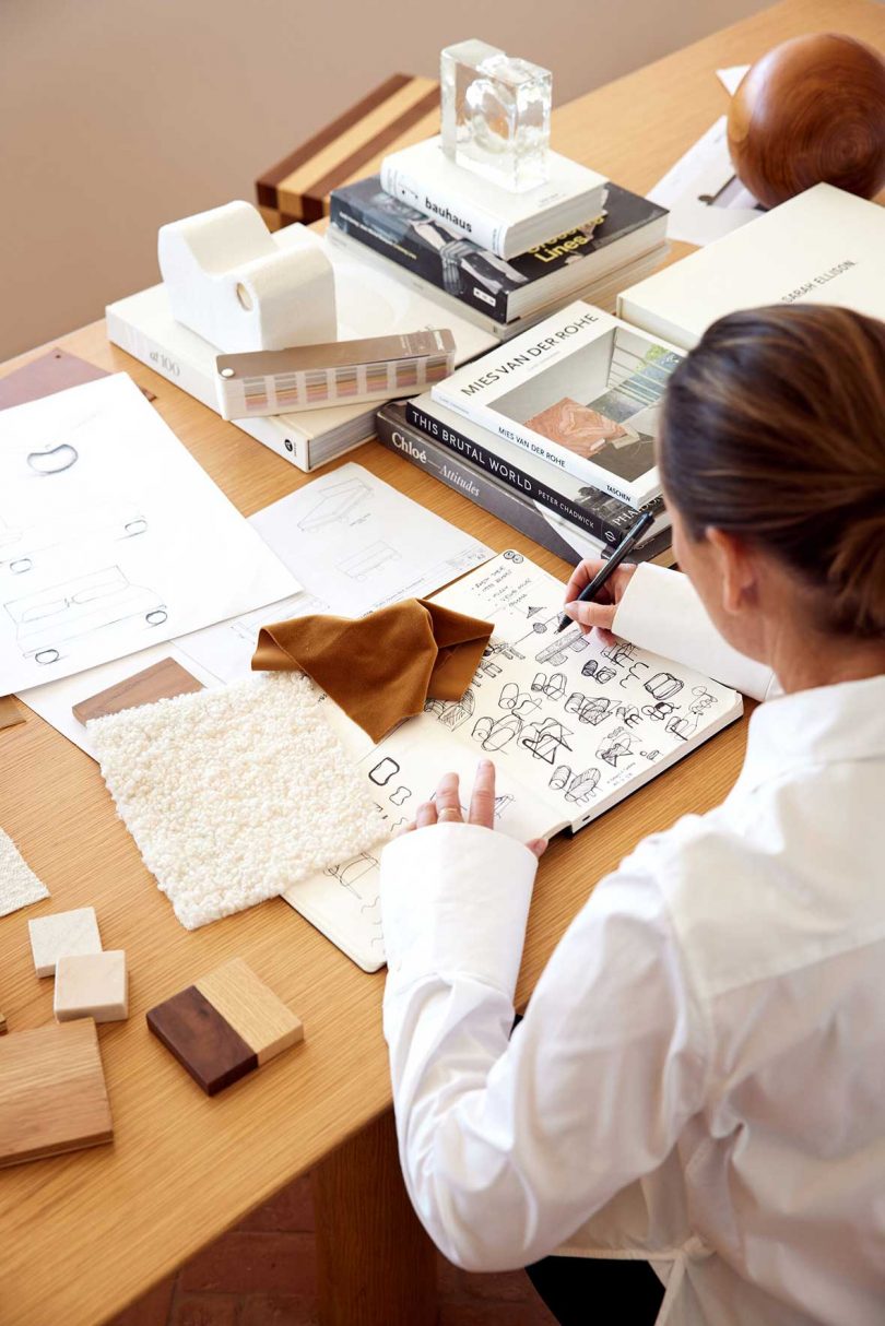 high angle view of designer at desk drawing in notebook with textile sample around