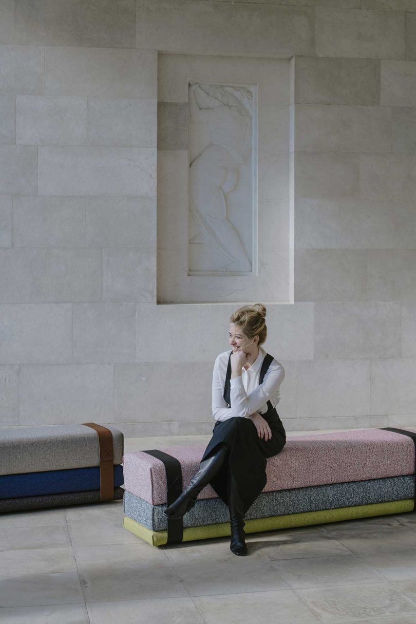 light-skinned woman sitting on upholstered settee in marble-covered space