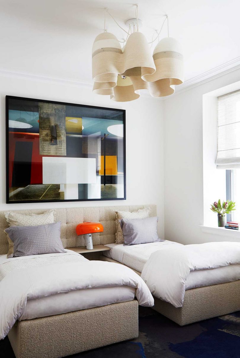 bedroom with two beds dressed in light colors and abstract light fixture