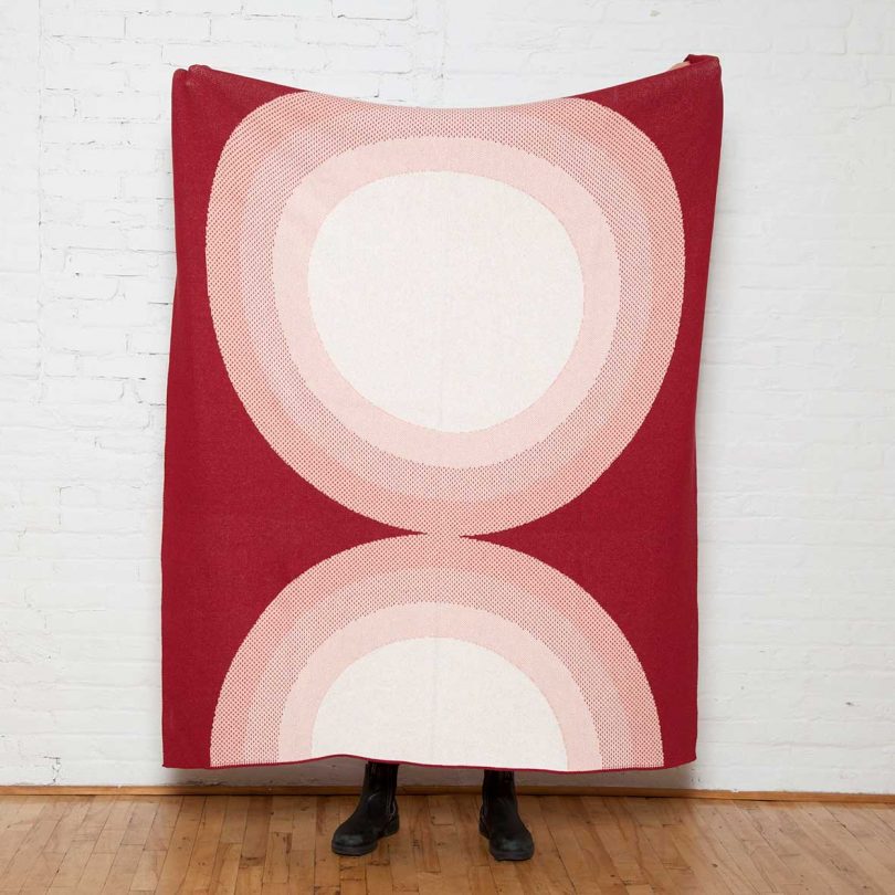person holding up throw blanket that's rust colored with concentric circles in pinks