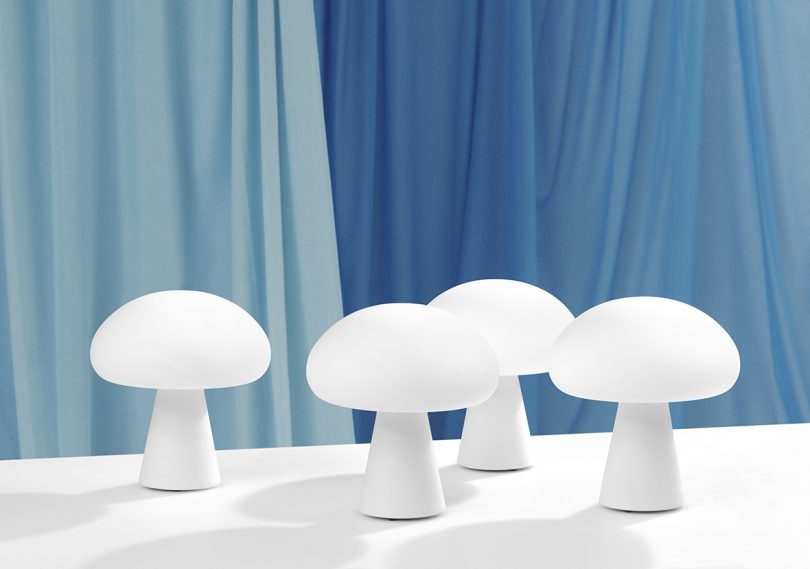 four white mushroom-shaped table lamps on white surface in front of blue fabric background