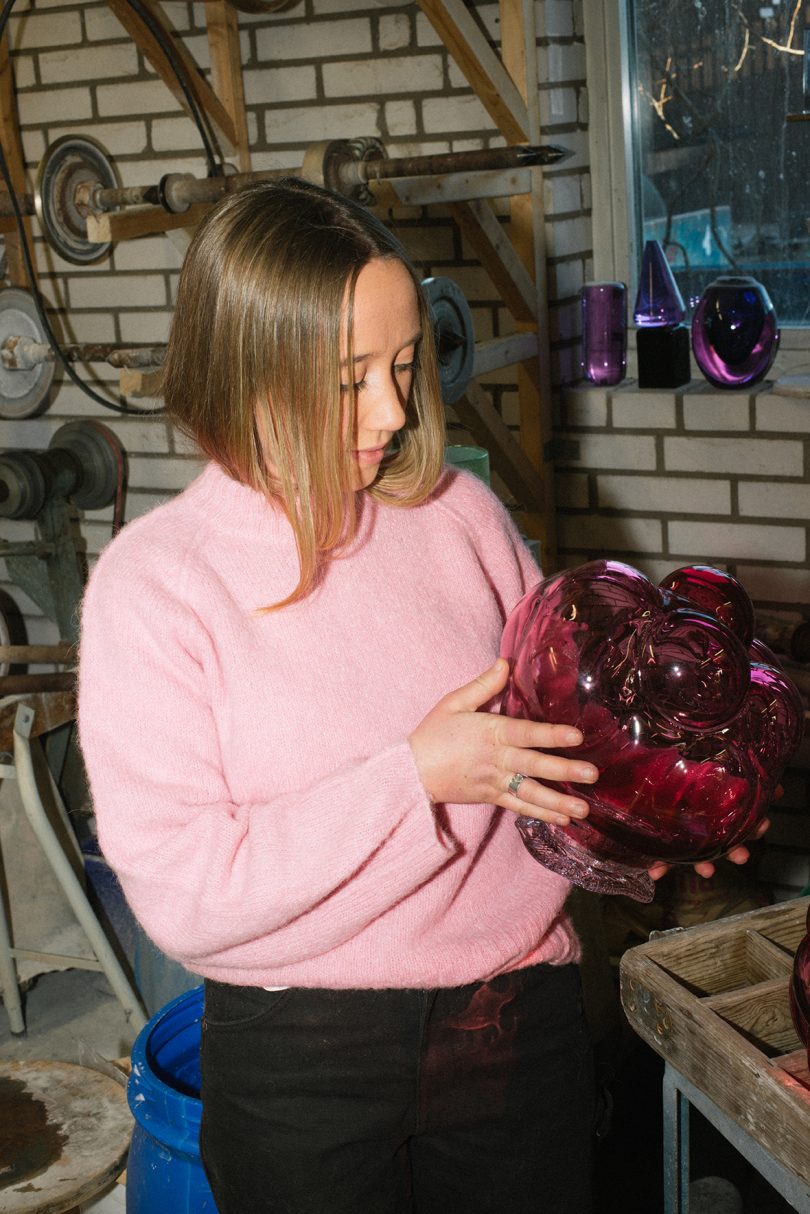 light-skinned woman inspecting a glassblowing project in dark studio space