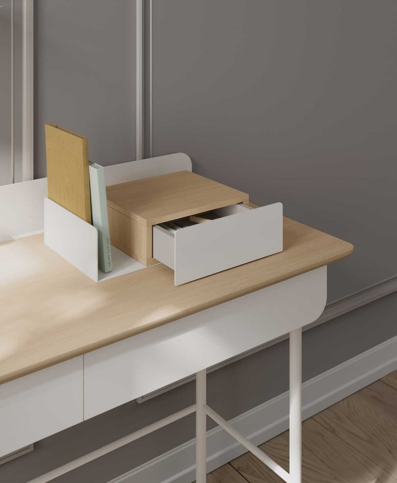 detail of styled white and light wood desk with open drawer in front of light grey wall