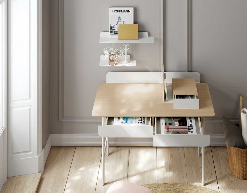styled white and light wood desk with open drawers in front of light grey wall
