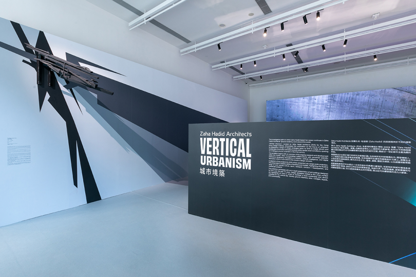 exhibition entrance with black wall reading VERTICAL URBANISM in white
