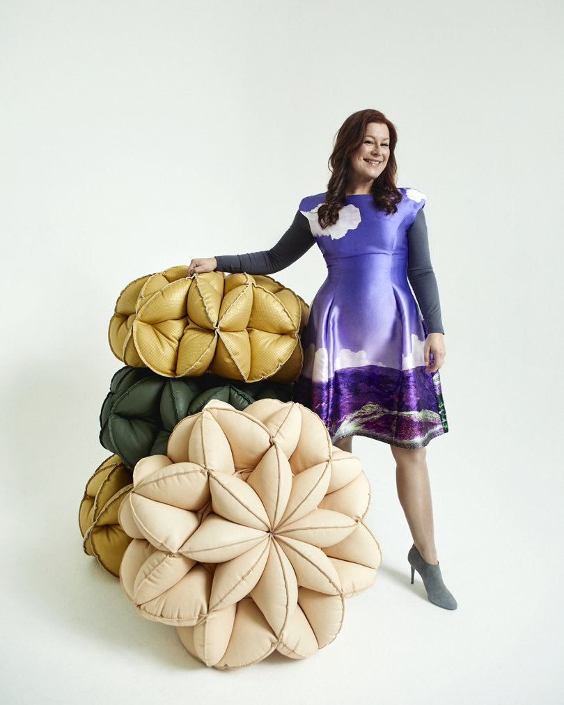 light-skinned woman wearing a purple dress and heels posing with four stacked poufs
