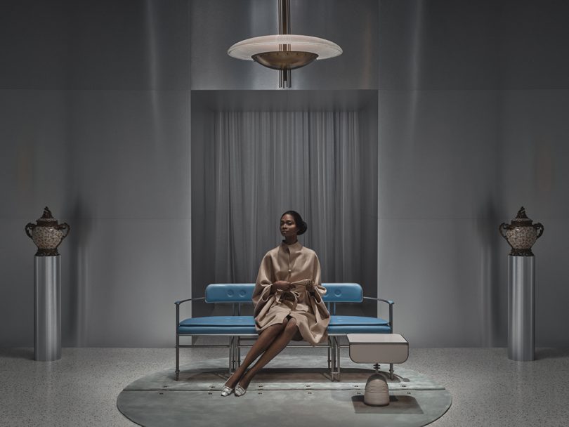 staged space with light blue upholstered bench, chandelier, side table, and floor rug with dark-skinned woman sitting on bench