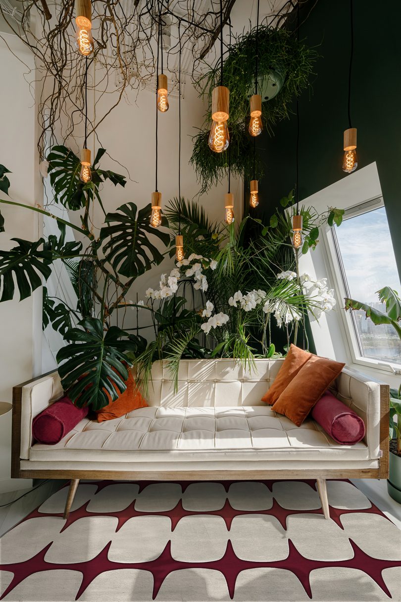 Vertical shot of light cozy boho style living room with modern beige sofa and orange pillows in relaxing area, decorated with different green plants