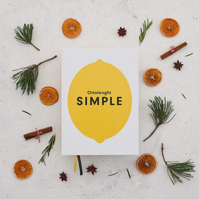 cookbook with illustrated lemon on the cover surrounded by orange slices, cinnamon sticks, and piece of pine on a white background