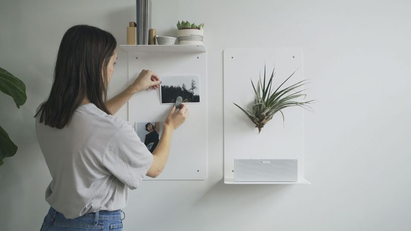 woman hanging two white memo board shelves on white wall