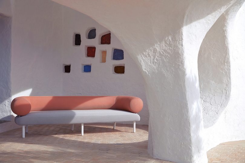 roll back and arm white and coral colored outdoor sofa in an alcove