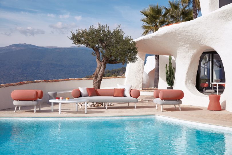 roll back and arm white and coral colored outdoor sofa, chairs, and coffee table next to a pool
