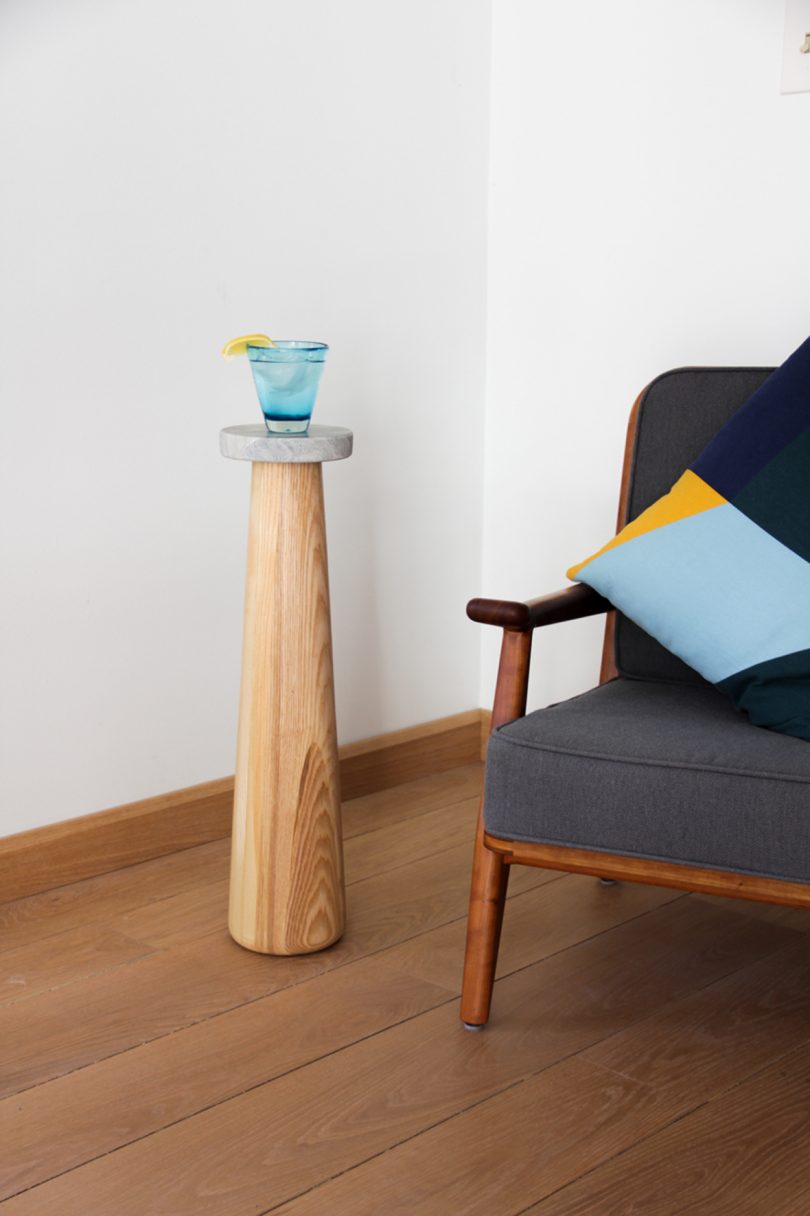 slim wood and marble drink stand holding a drink next to armchair