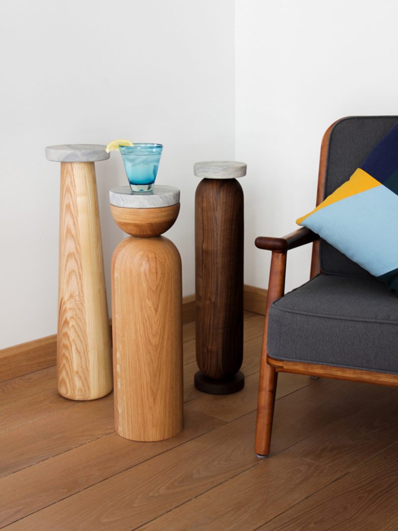 slim wood and marble drink stands holding a drink next to armchair