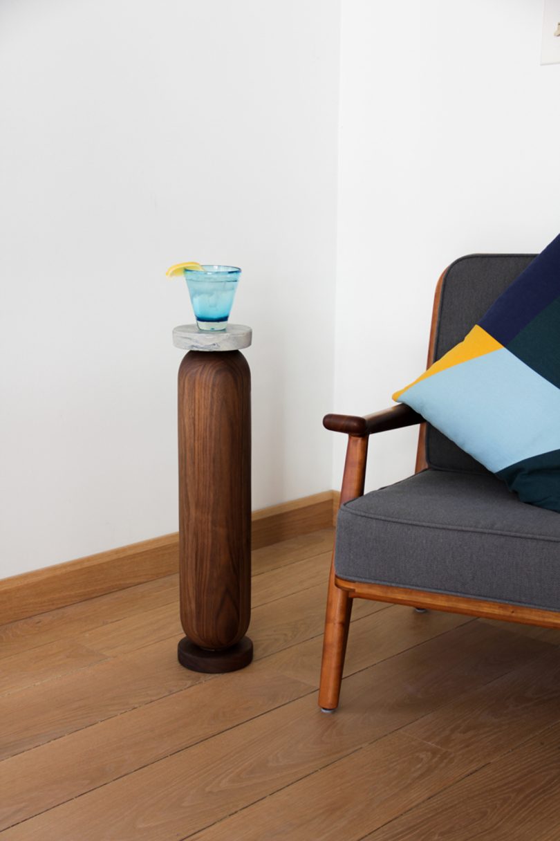slim wood and marble drink stand holding a drink next to armchair