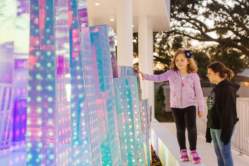 little girl interacting with iridescent pillar sculpture