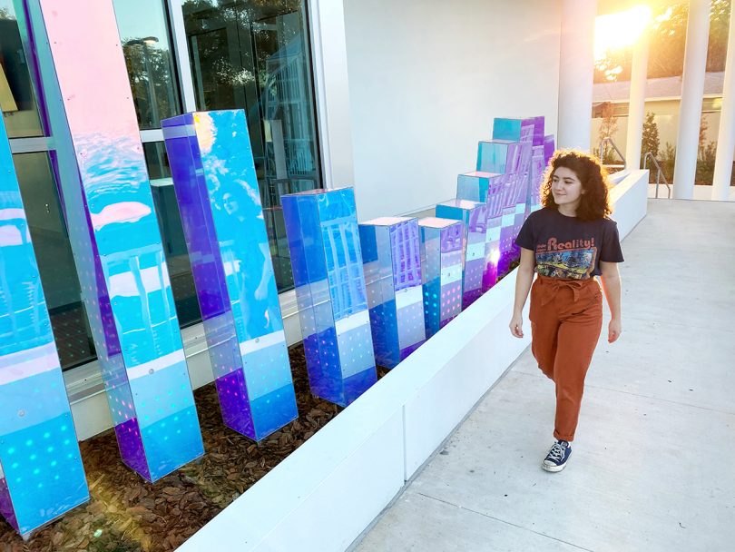 woman walking next to iridescent pillar sculpture