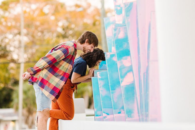 man and woman interacting with iridescent pillar sculpture