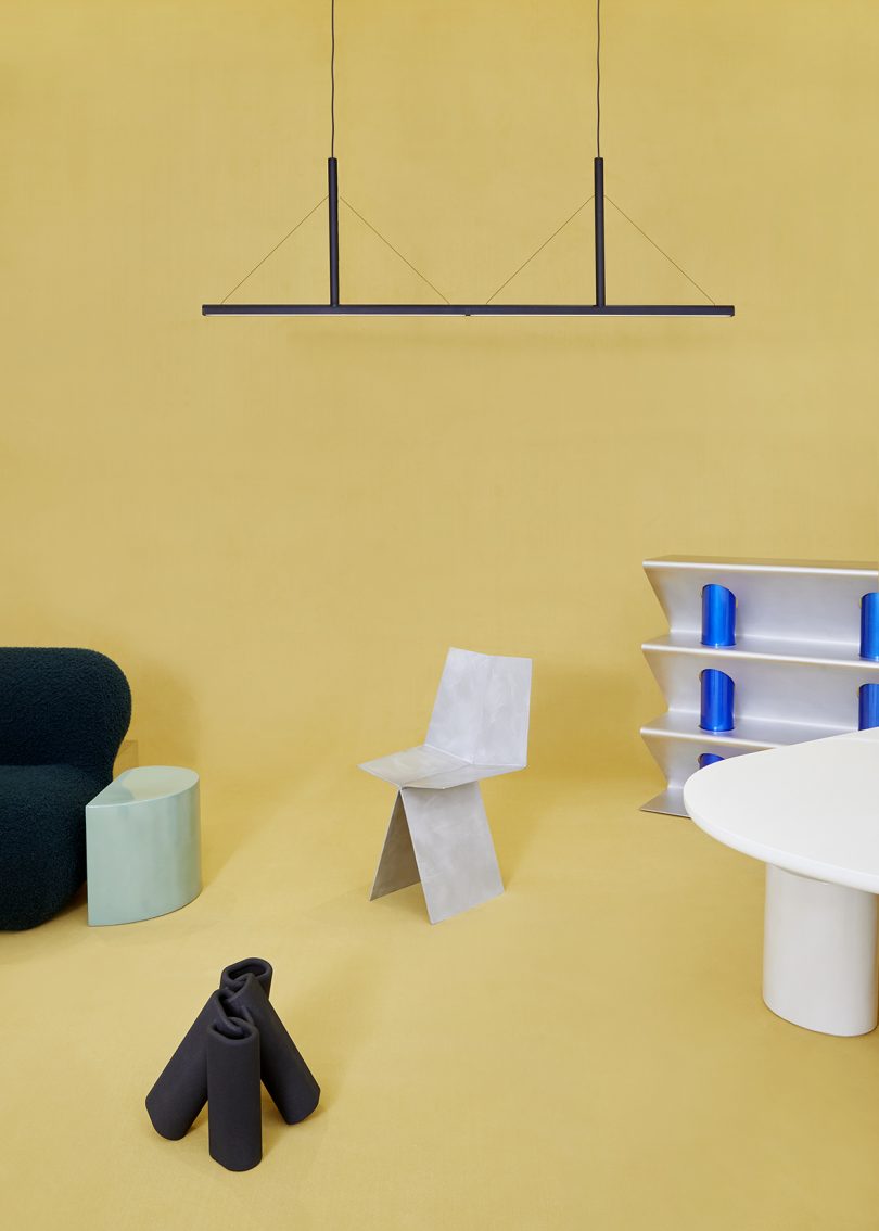 side table, chair, sculpture, dining table, shelves, and light fixture on butter yellow background