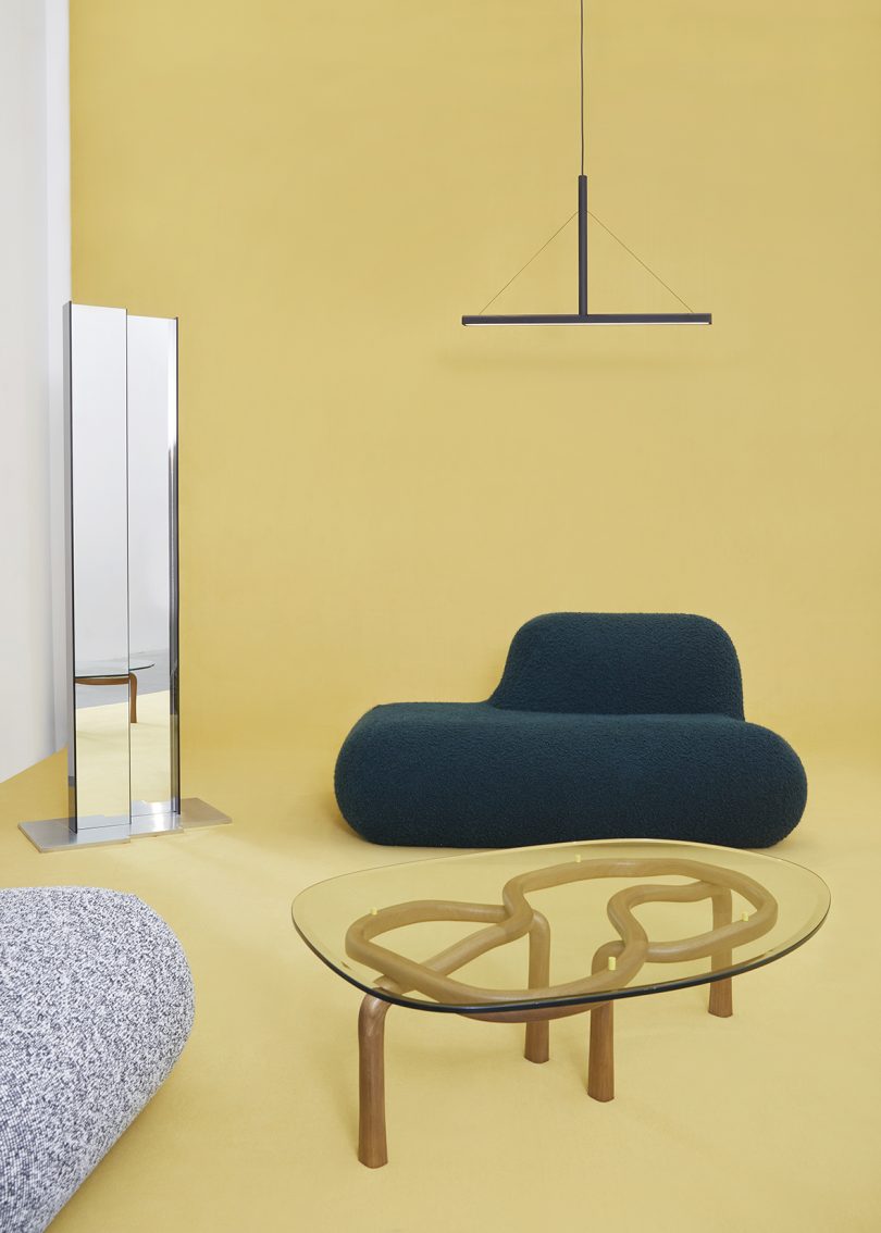 tall mirror, dark green chair, glass topped coffee table, and lighting on butter yellow background