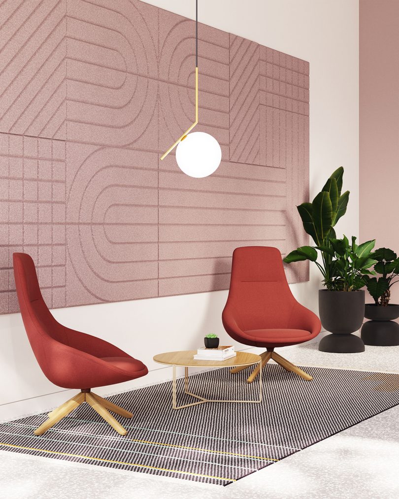 two red lounge chairs with coffee table and pendant lamp in front of a pink wall
