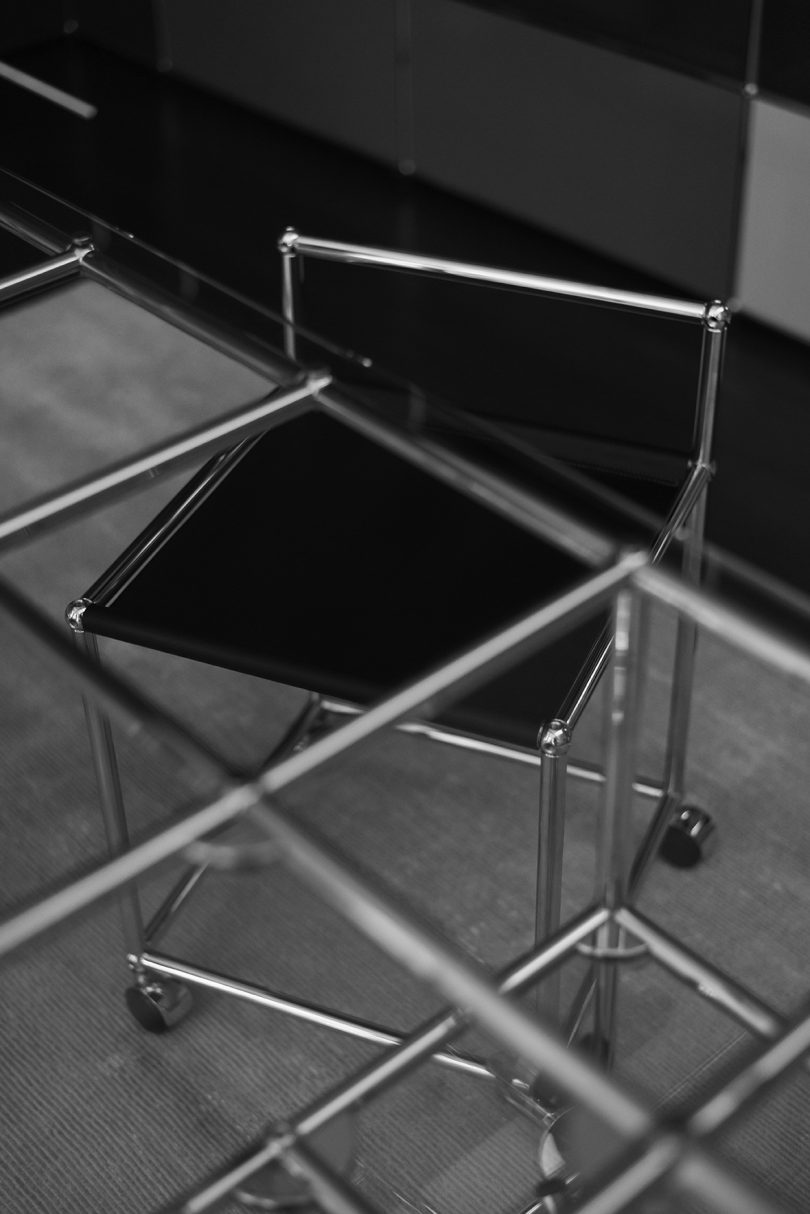 Silla sling negra con estructura de metal bajo cristal y escritorio de metal
