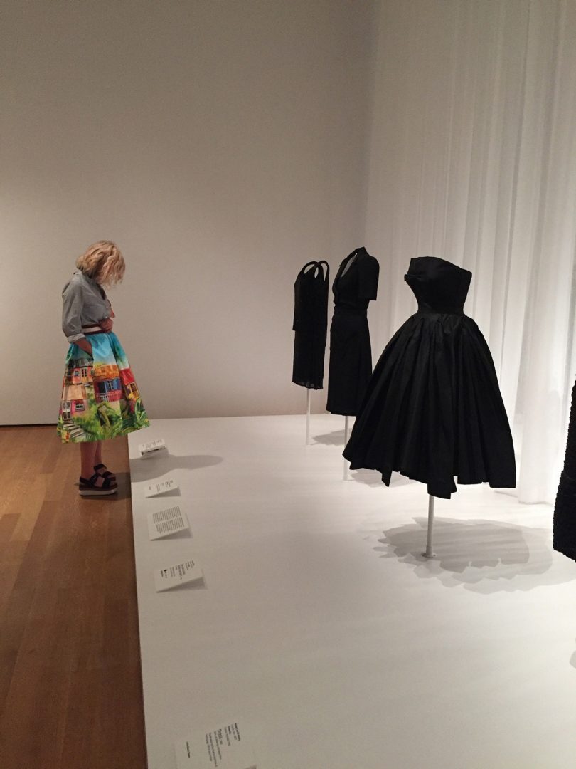 man looking at four black clothes in a museum-like space