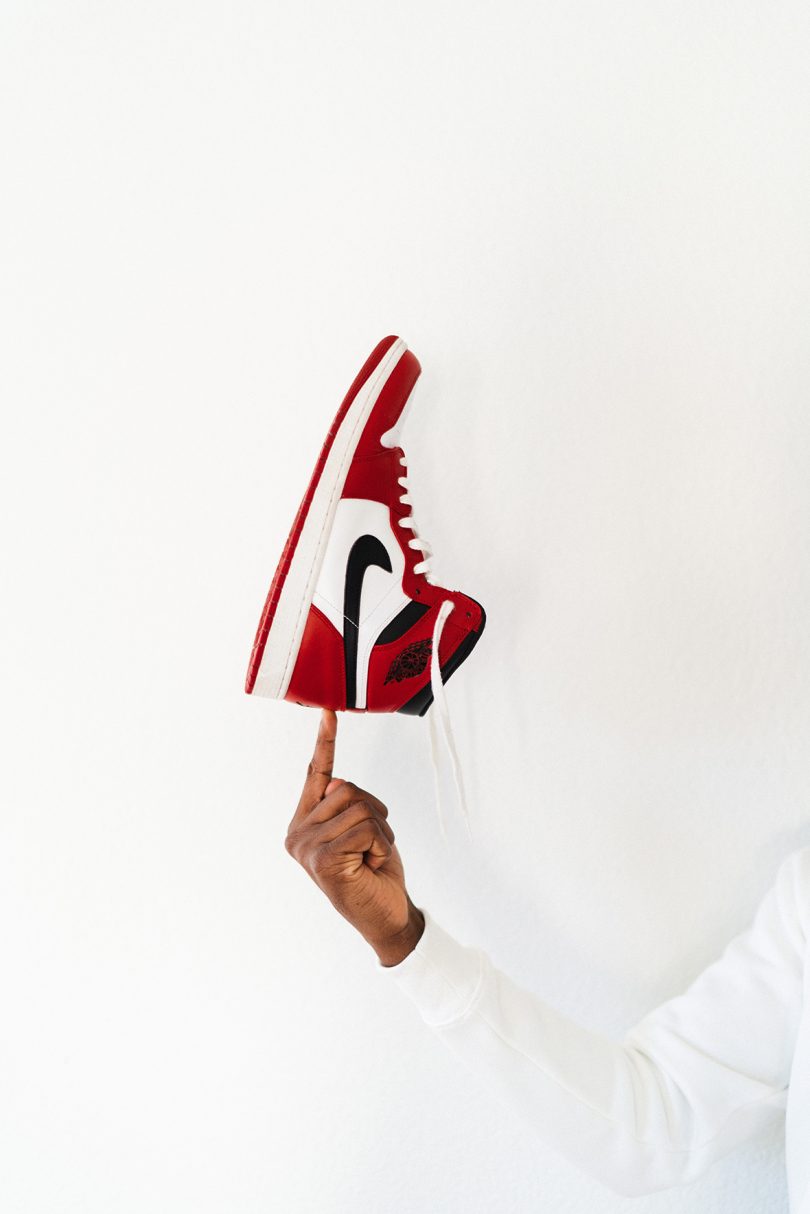 Brown-skinned hand balancing a Nike sneaker on a finger against a white background.