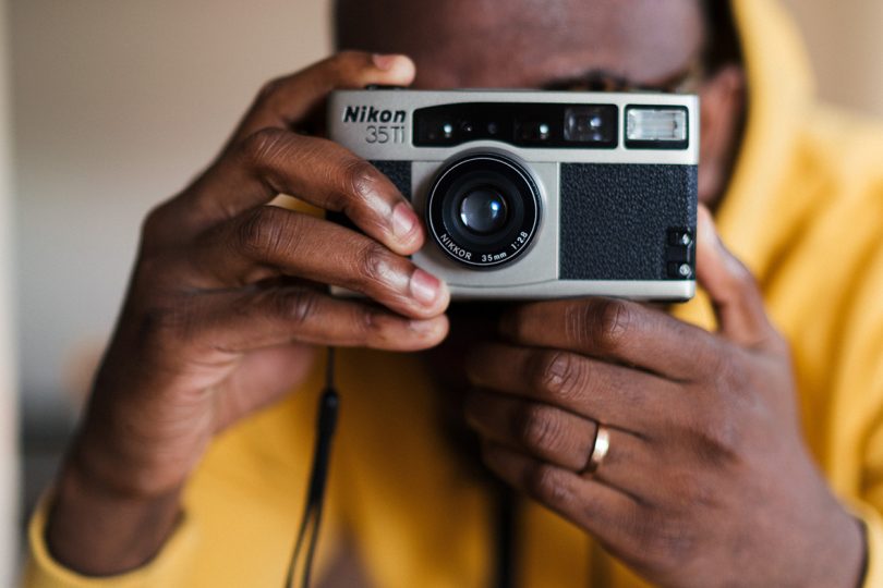 brown-skinned person holding and looking through a 35mm camera