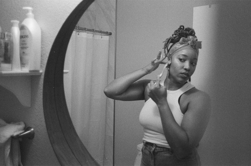 black and white image of dark-skinned woman primping in a bathroom mirror