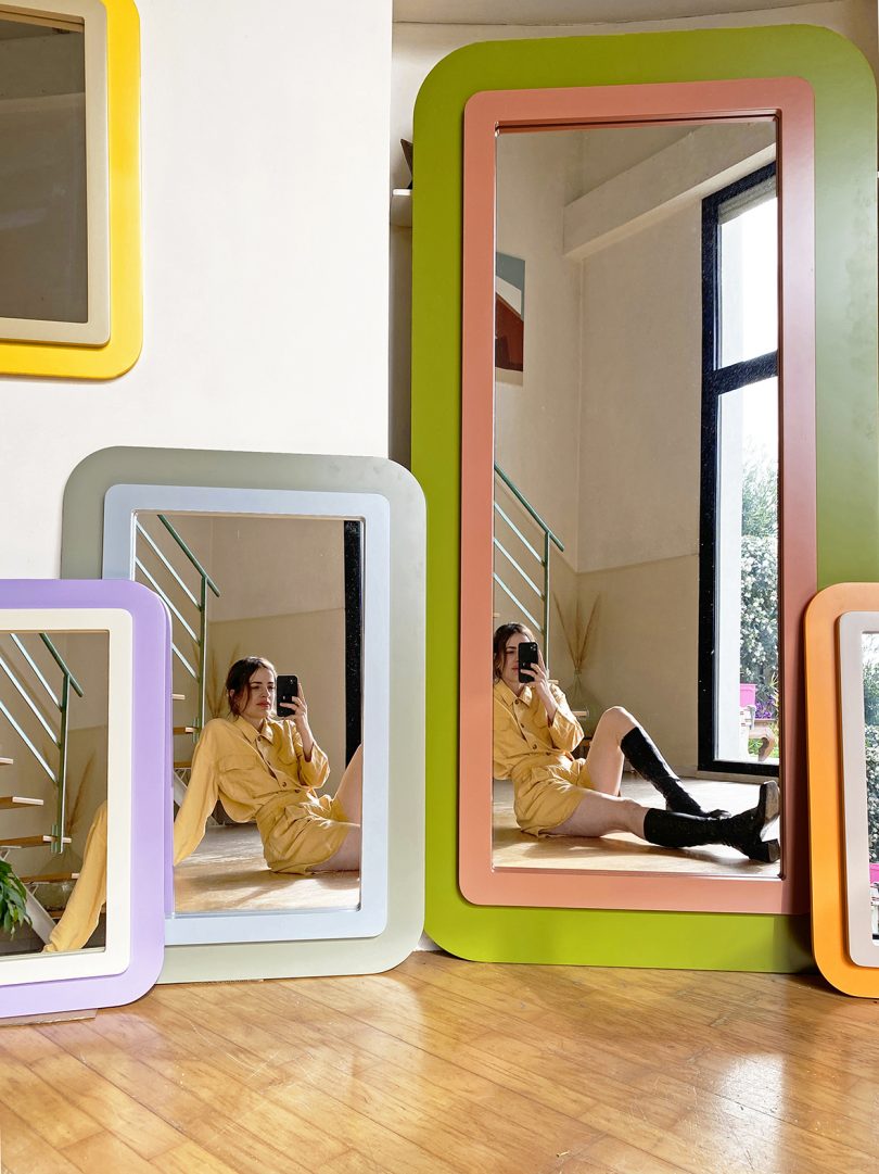 light-skinned woman with dark hair reflected in a selection of colorful mirrors