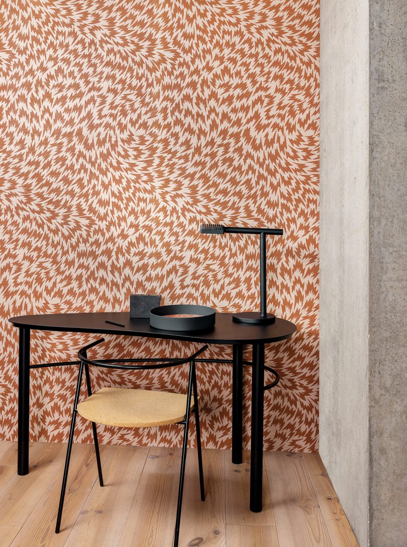 black corner desk with chair and light against patterned wallpaper