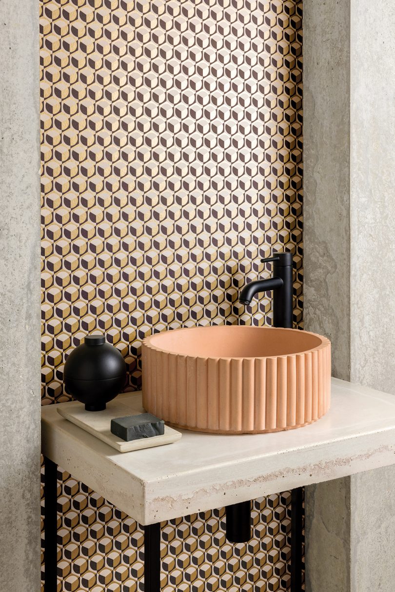 modern terra cotta sink with black faucet in front of patterned wallpaper
