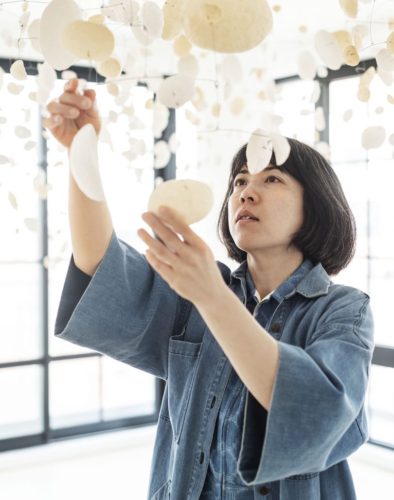 artist with art installation of suspended white disks in white room