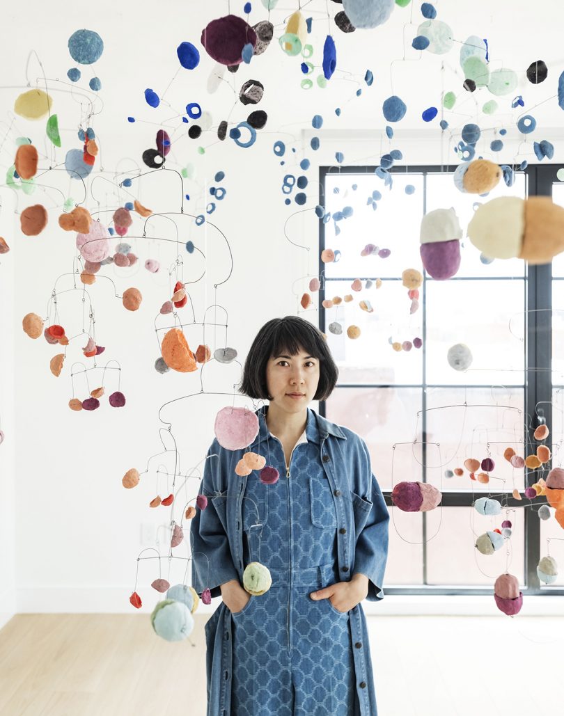 artist with art installation of suspended colored disks in white room