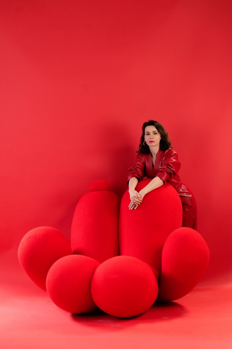 light-skinned woman wearing all red leaning on bulbous red armchair on red background