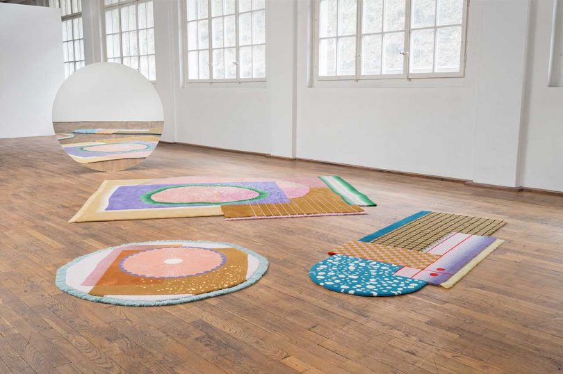three bold irregular rugs lay on a wood floor in a white room