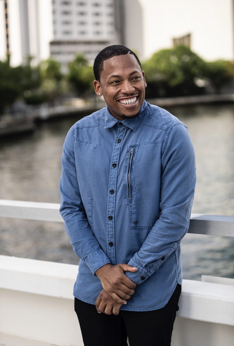 dark-skinned man wearing a blue button down shirt and smiling