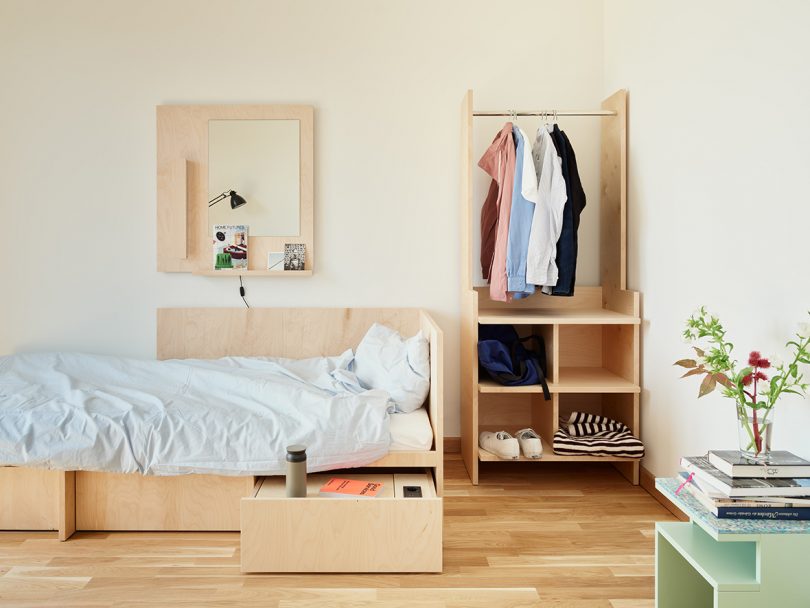 college dorm space with modern light wood bed, mirror, and wardrobe