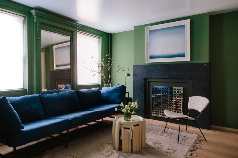 living space with olive green walls, blue sofa, chair, small table, fireplace, and art