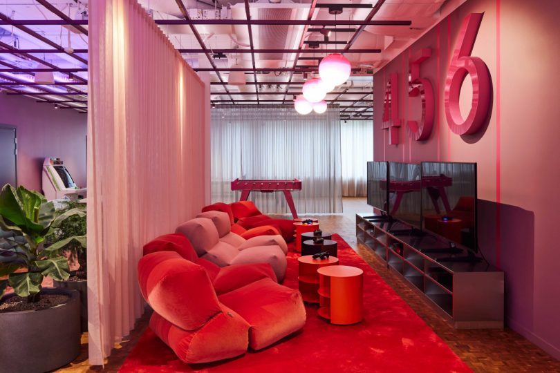 sitting area of modern office interior with pink/red plush seating in front of tvs