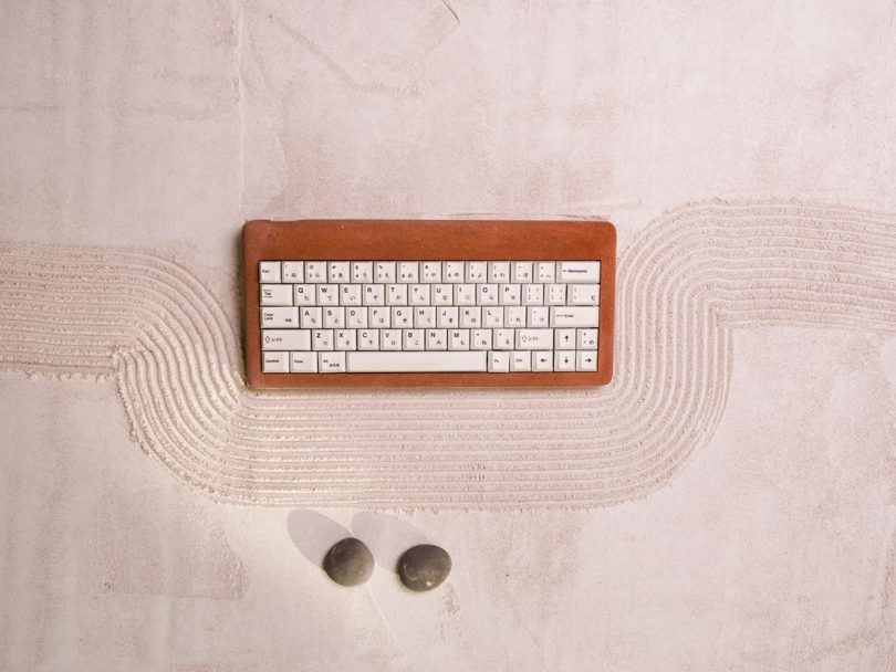 Brown stone keyboard with white keys against raked pink sand and two small stones.